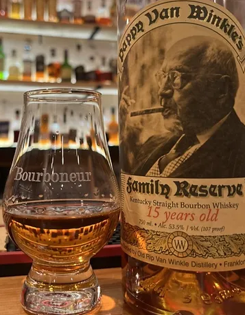 A glass of alcohol next to a bottleDescription automatically generated